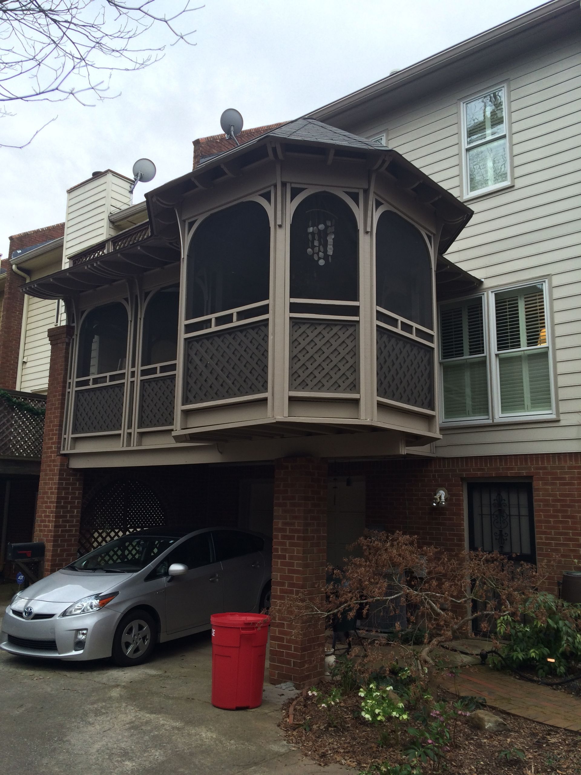 A car is parked under a screened in porch in front of a house.