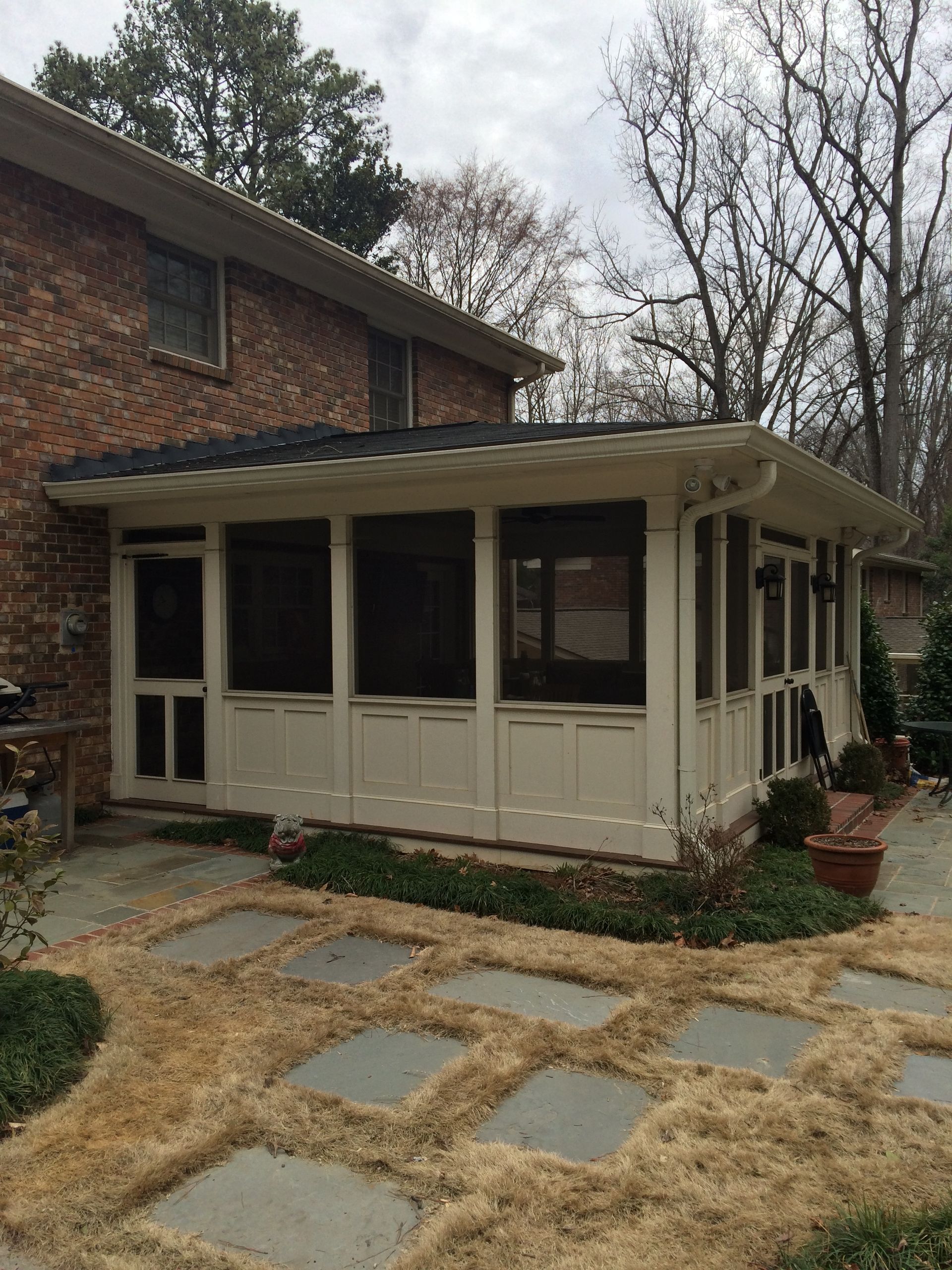 A screened in porch with a brick house in the background