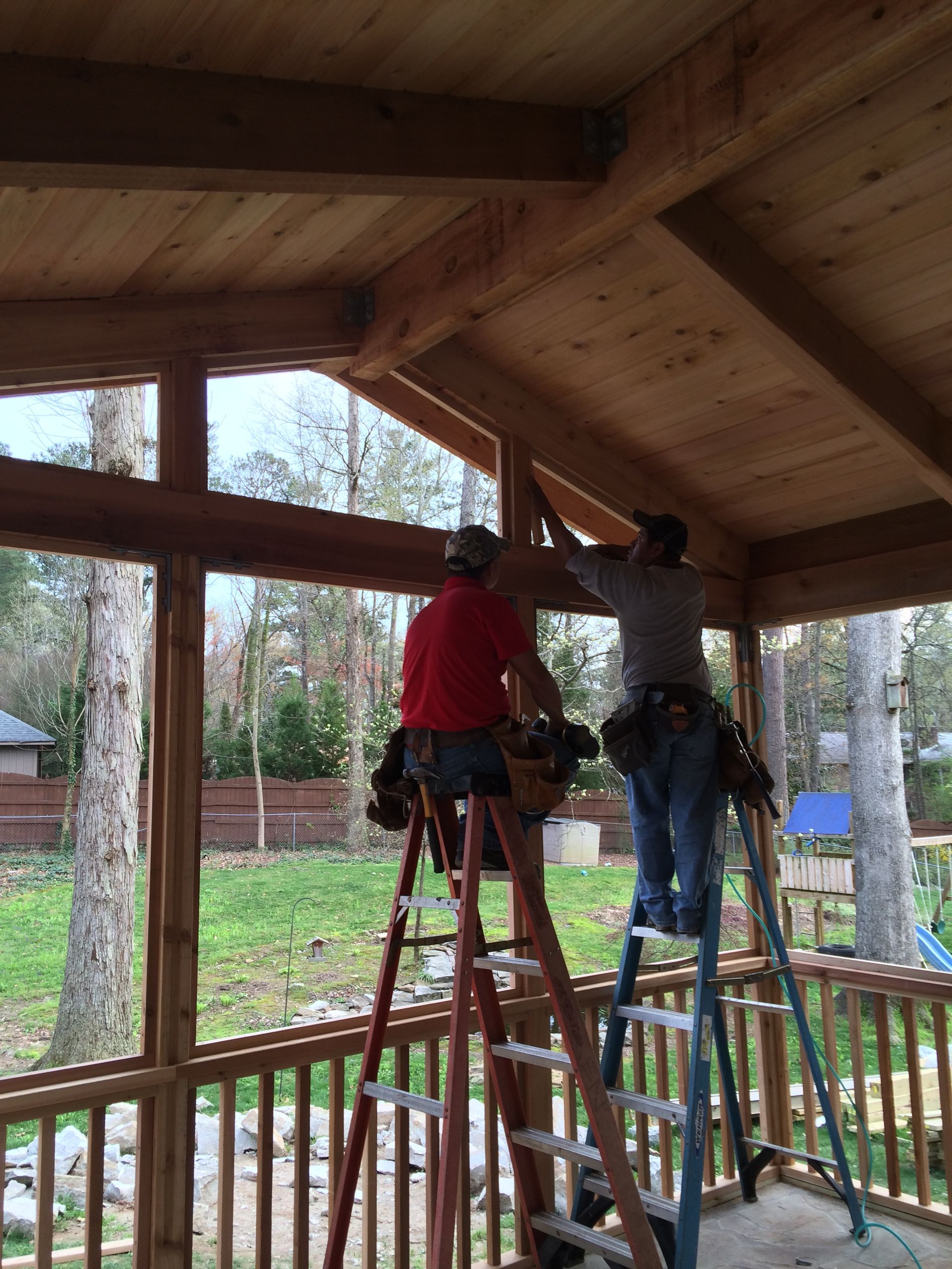 Two men are standing on a ladder working on a wooden structure.