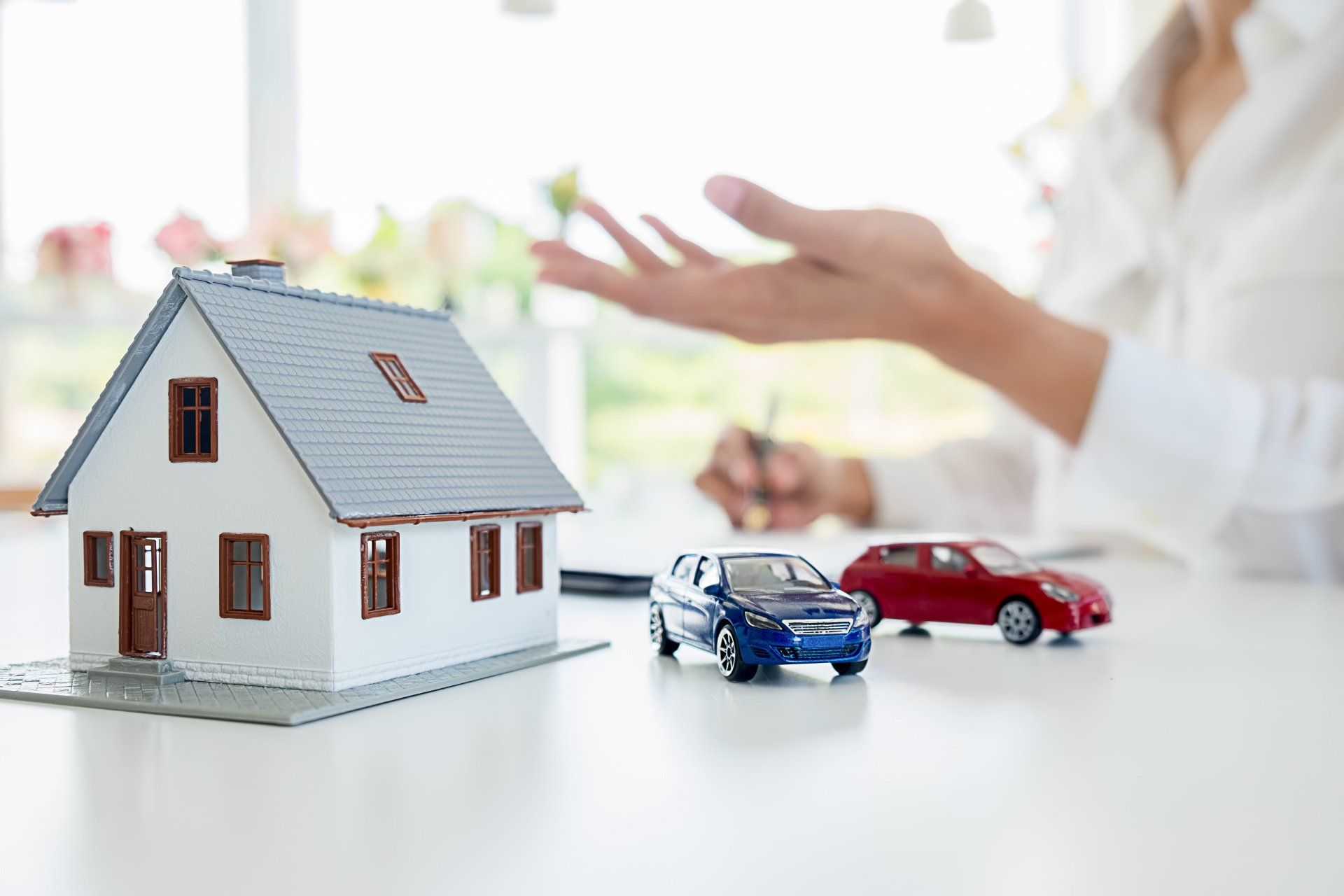 A woman is sitting at a table with a model house and two toy cars.