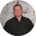 A man in a black shirt is smiling in front of a map.