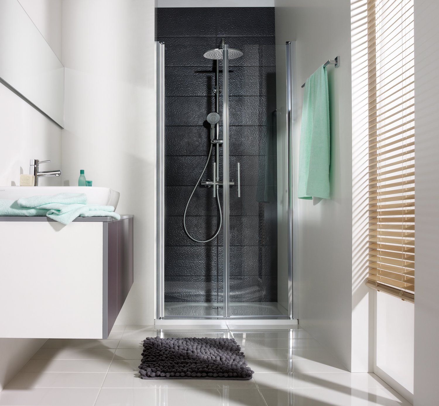 Kleines Badezimmer mit Waschbecken und Dusche in Raumnissche mit schwarzen Wandfliesen