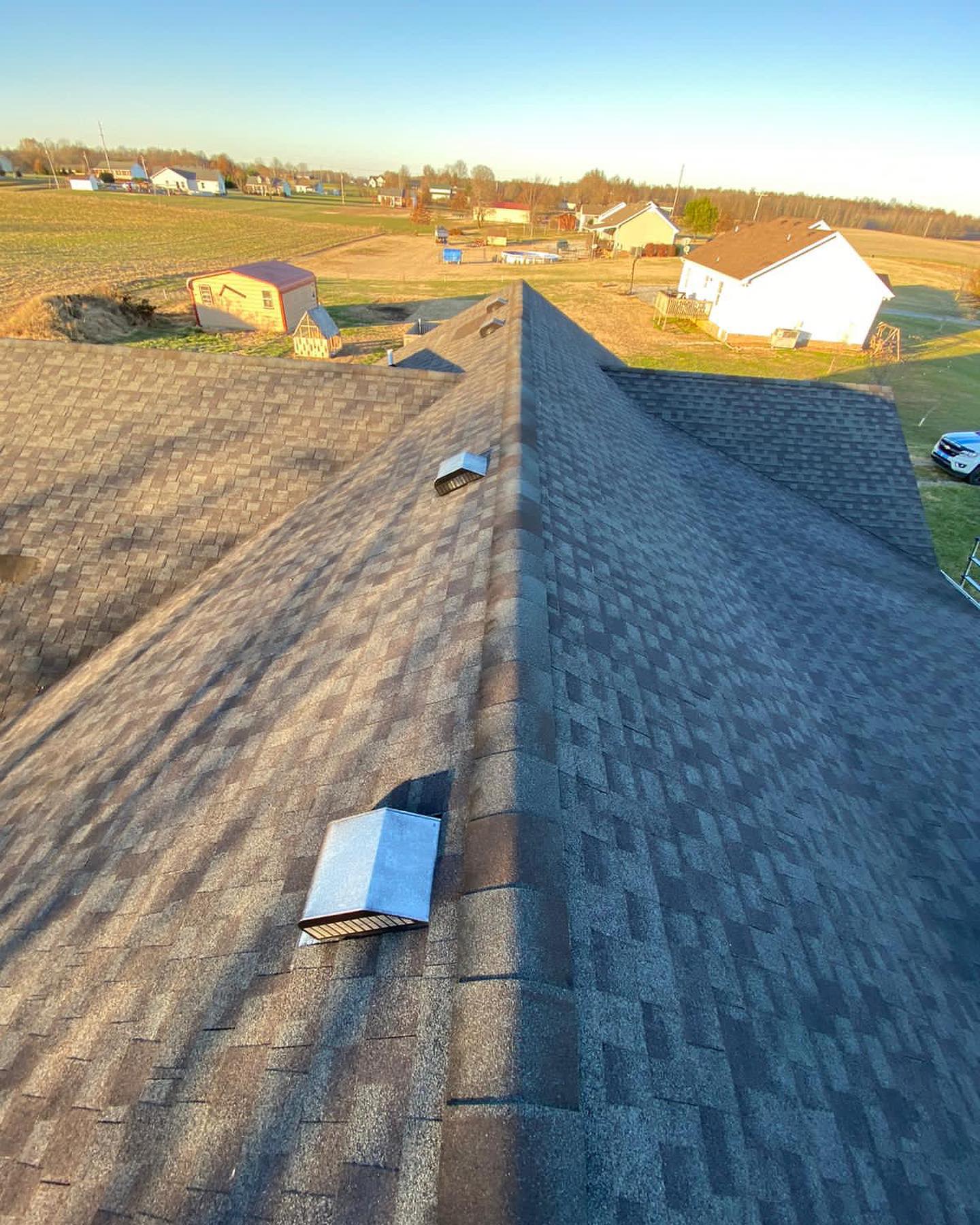 Rooftop with gray shingles and skylights, overlooking a sunlit rural neighborhood at sunset