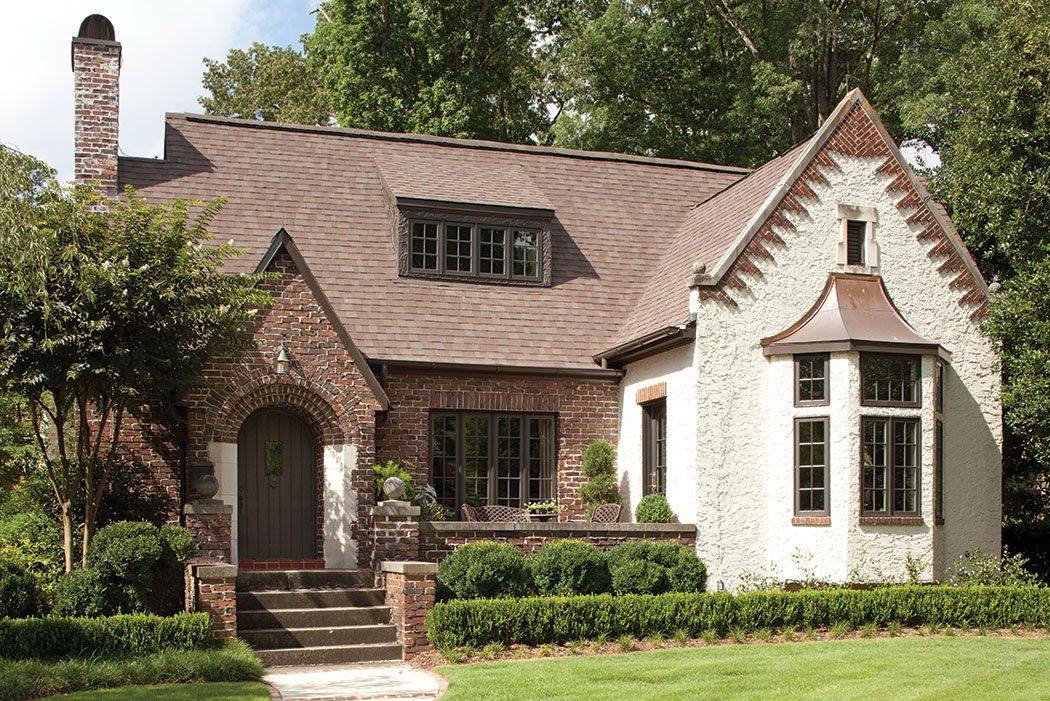 Brick cottage with white-trimmed gables, front steps, and a green lawn under trees