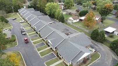 Aerial view of a row of gray-roofed townhouses with driveways and parked cars in a suburban neighborhood