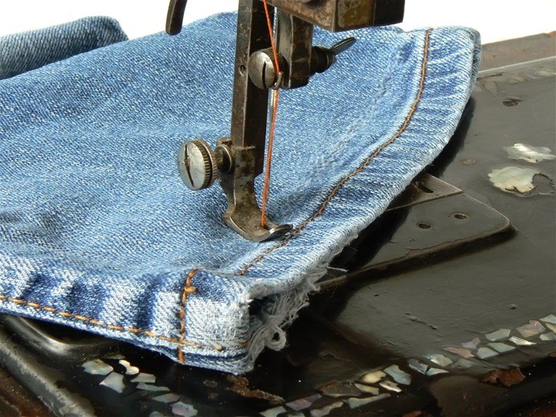 A sewing machine is working on a pair of blue jeans