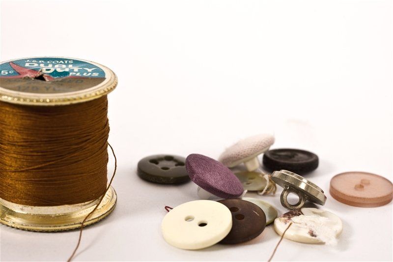 A spool of brown thread and buttons on a white surface