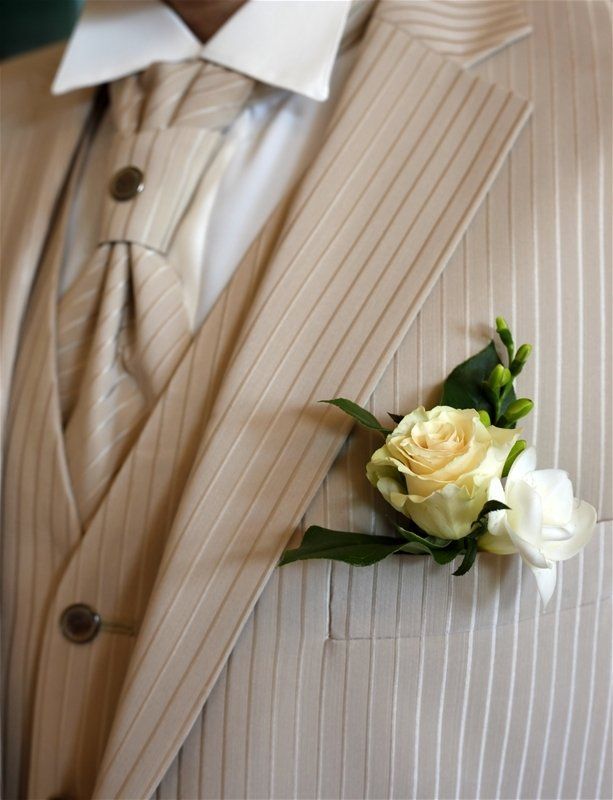 A man in a tan suit has a white rose in his pocket