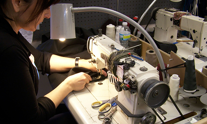 A woman is working on a sewing machine with a bottle of water in the background