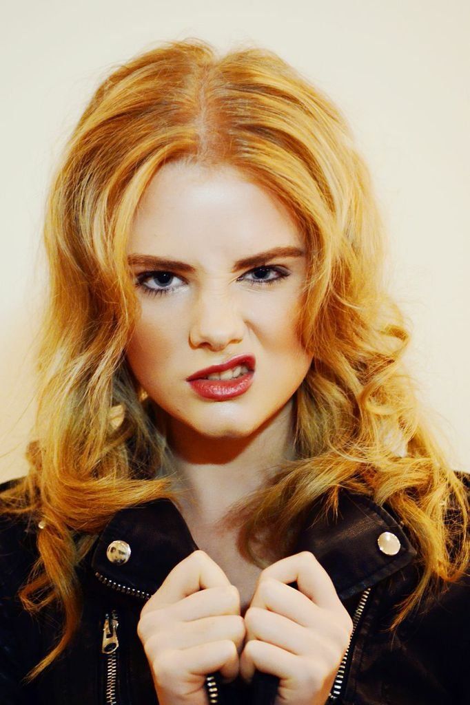 A woman with red hair is wearing a black jacket and making a funny face