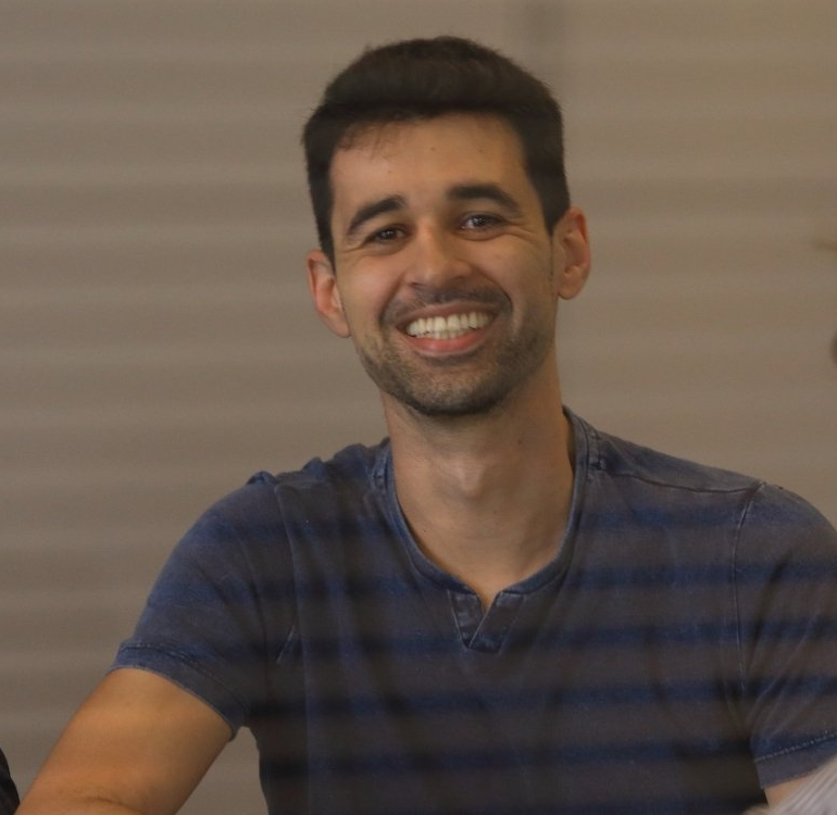 Um homem com uma camisa listrada azul está sorrindo para a câmera