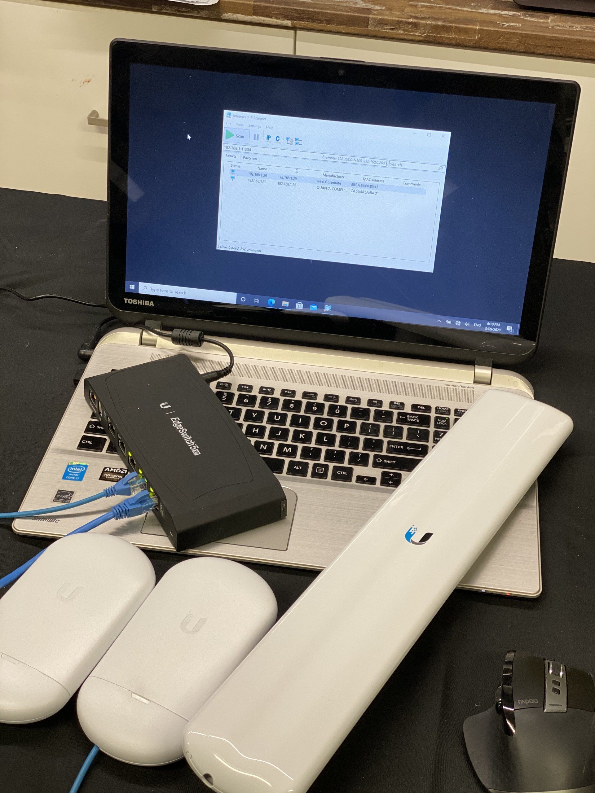 A laptop is sitting on a table with a wireless access point and switch on it