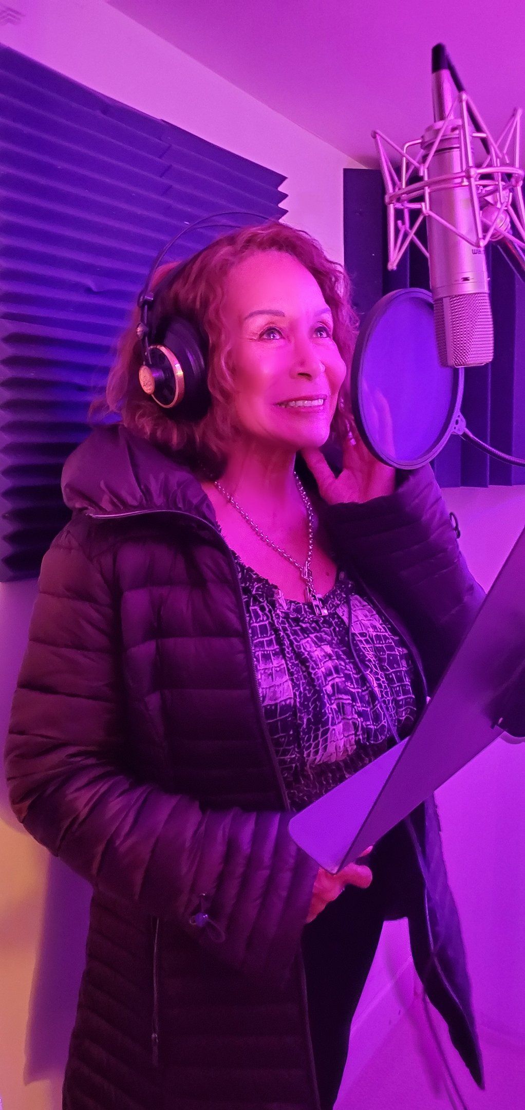 Woman wearing headphones sings into a studio microphone under purple lighting
