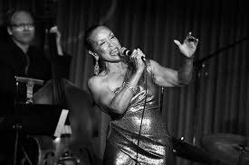 Singer performing onstage in a shimmering dress, holding a microphone under dramatic lighting