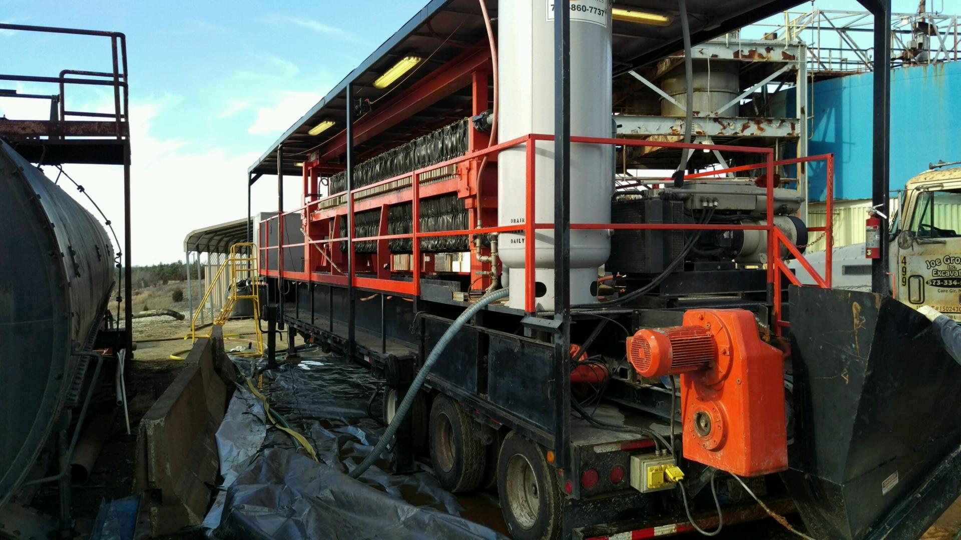 A truck with a hose attached to it is parked next to a large tank.