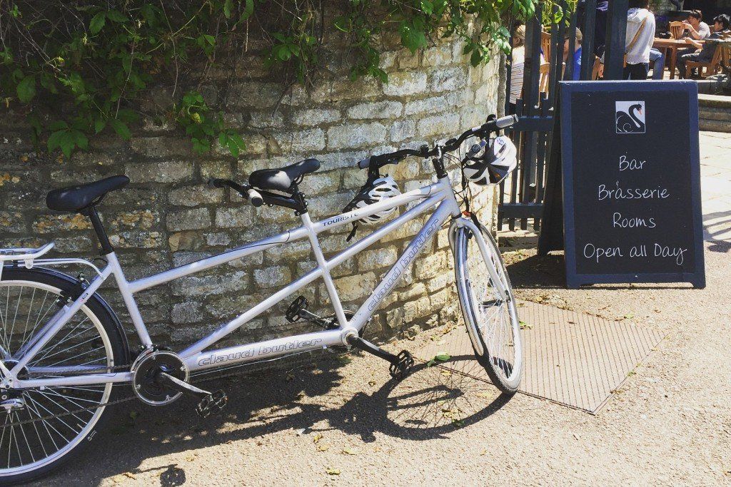 A tandem bike is parked in front of a brick wall.