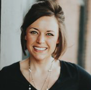 A woman wearing a black shirt and a necklace is smiling for the camera.