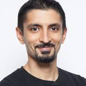 A man with a beard is wearing a black shirt and smiling for the camera.