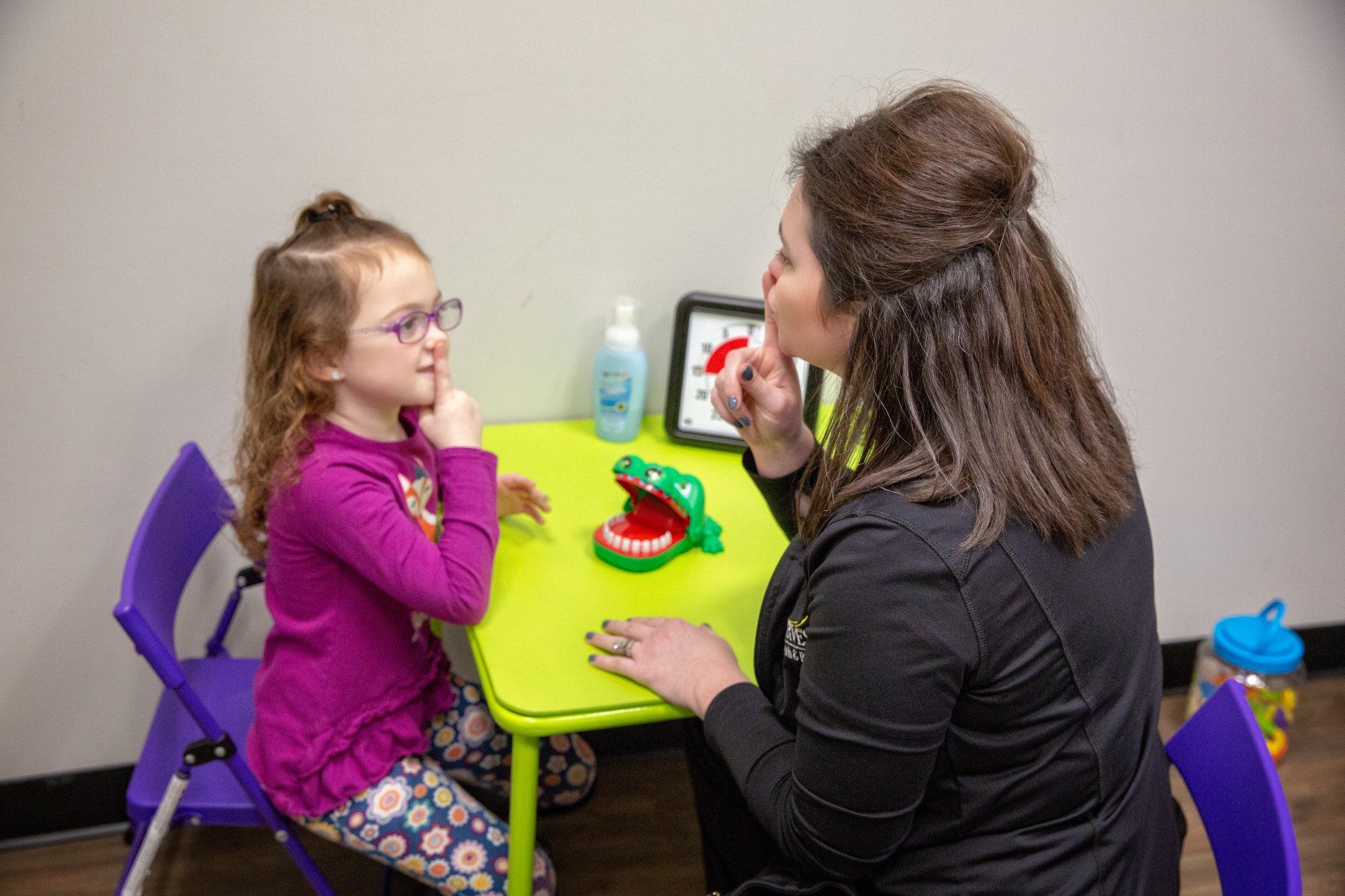 Woman and child seated at a small table in a playroom, talking over a toy tea set.