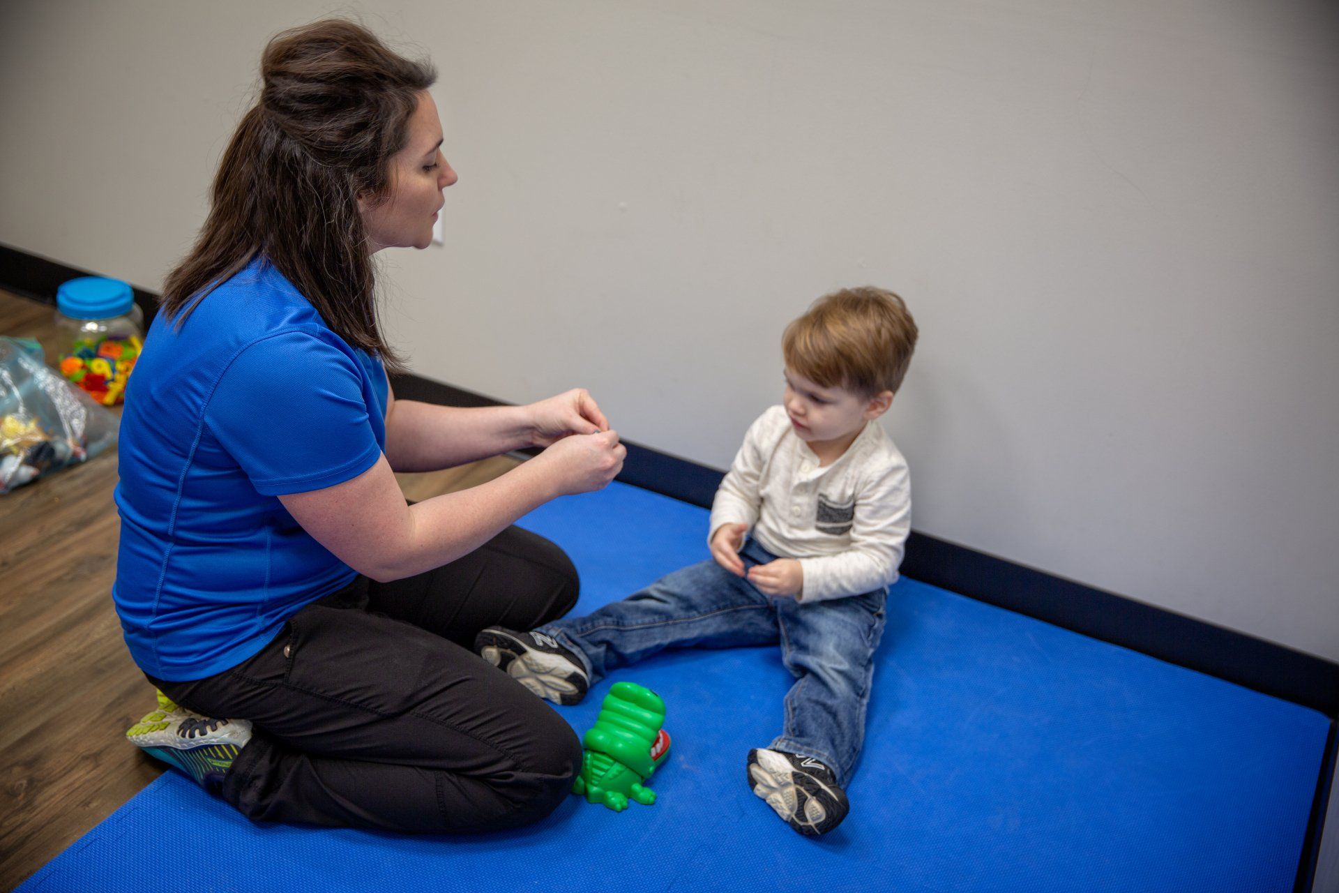 Adult and toddler sitting on blue mat during a play or therapy session indoors