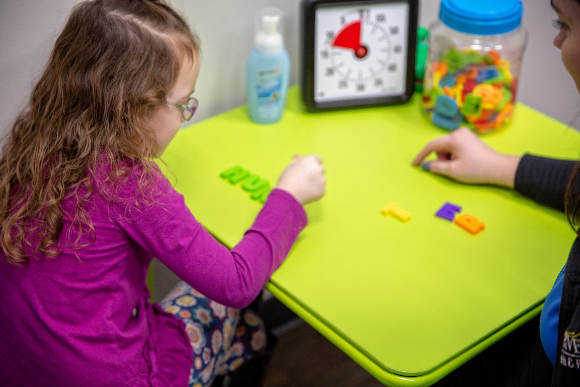 Children playing a color-matching game at a green table with blocks and a timer