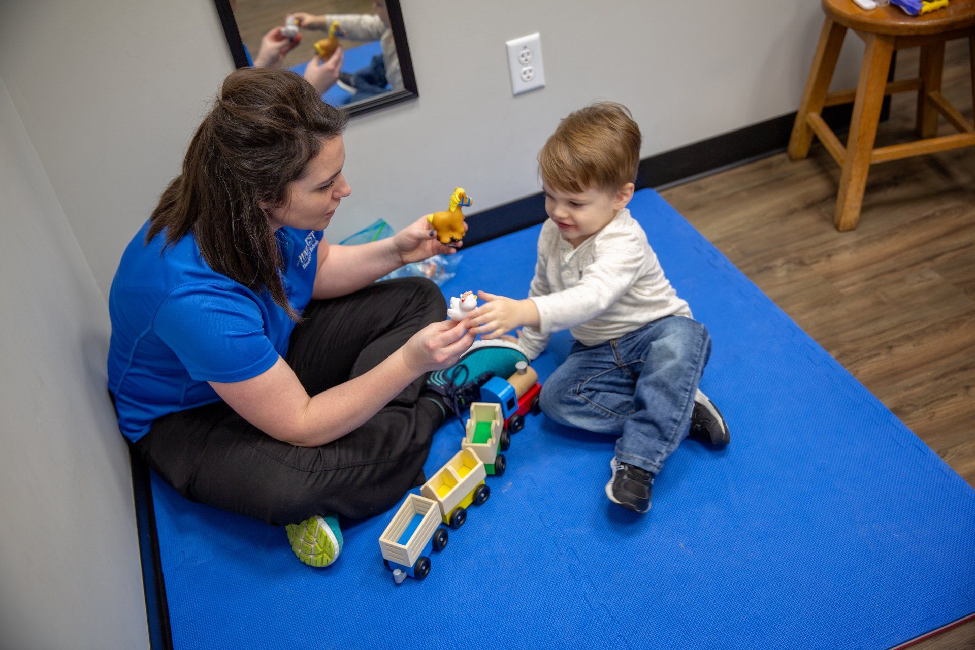Adult and child playing with toy train on a blue carpet in a small room
