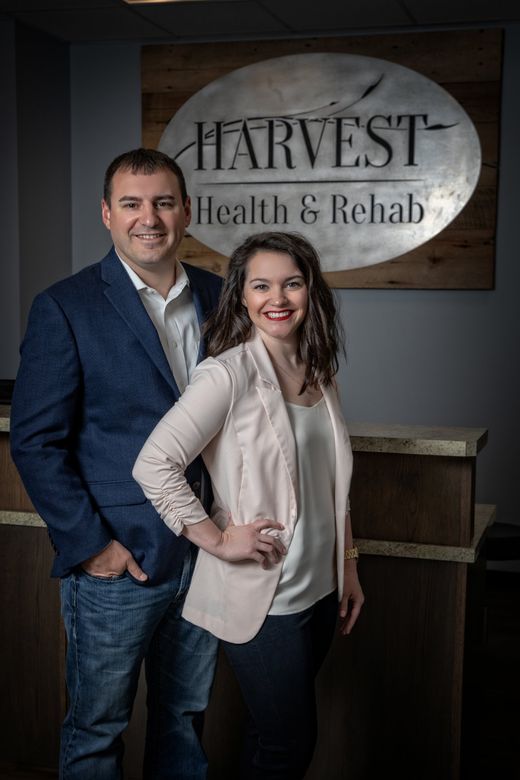 Two professionals posing in front of a Harvest Health & Rehab sign.