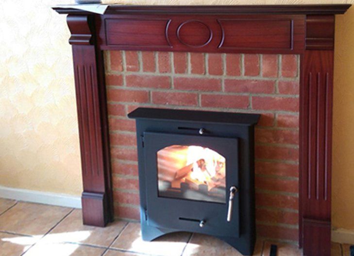 Wood burning stove in brick fireplace with wooden mantel and lit fire