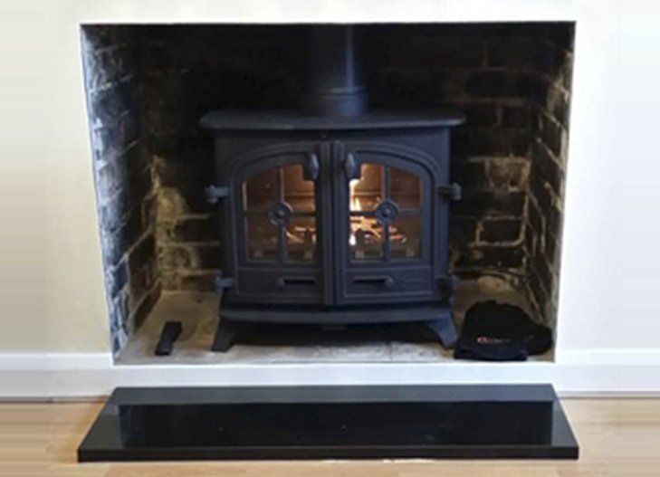 Double-door cast iron wood stove set inside a brick fireplace with black hearth