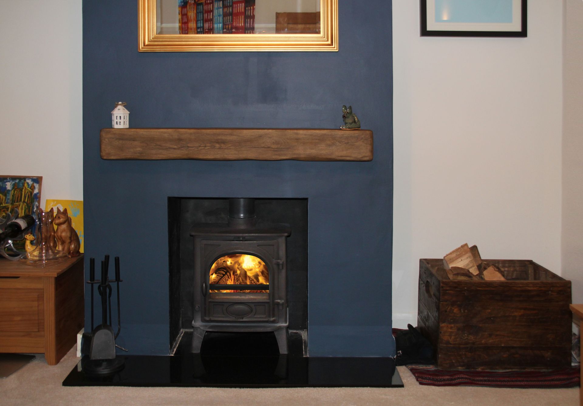 Wood-burning stove set in a blue feature wall with wooden mantel and log storage box