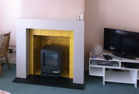 Wood burning stove in modern fireplace with yellow tiled interior and minimal living room setup