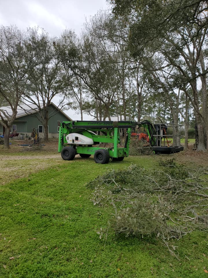 Green industrial vehicle parked on a grassy farm yard with trees, a house, and a trailer in the background