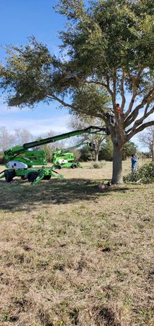 Green boom sprayer parked under a tree in a grassy field on a sunny day