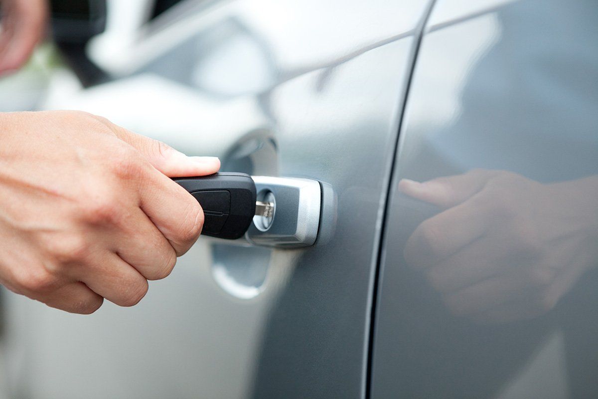 Hand turning a car key in a gray car door handle to unlock it.