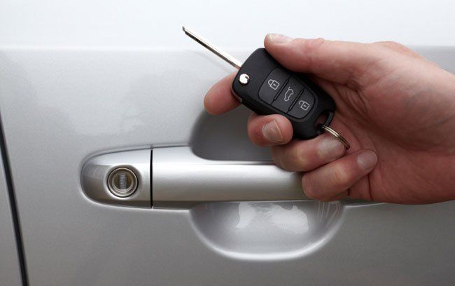 A person is holding a car key in front of a car door.