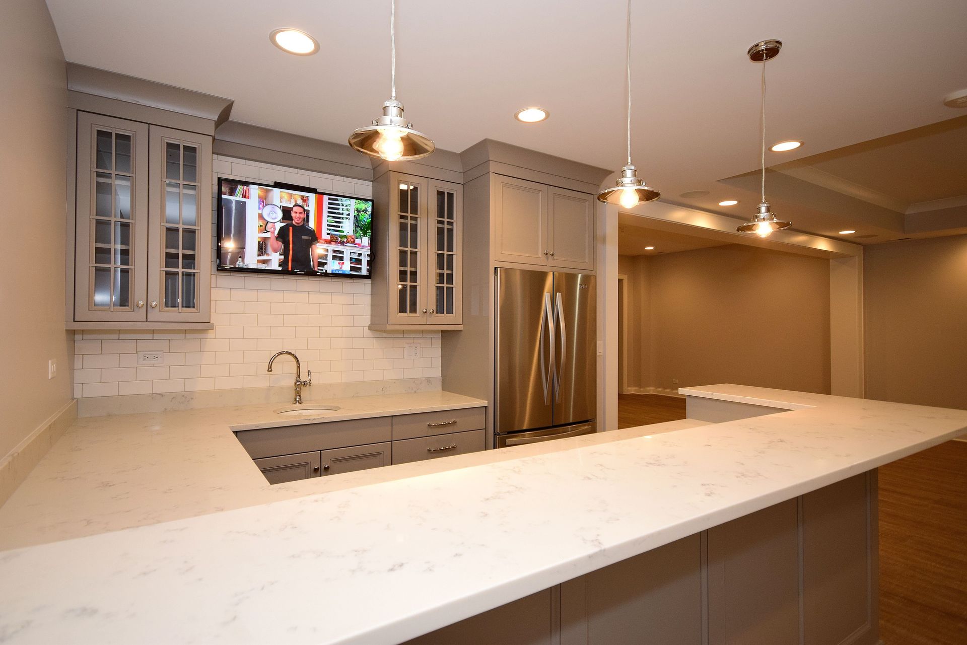 A kitchen with white counter tops and a flat screen tv on the wall.