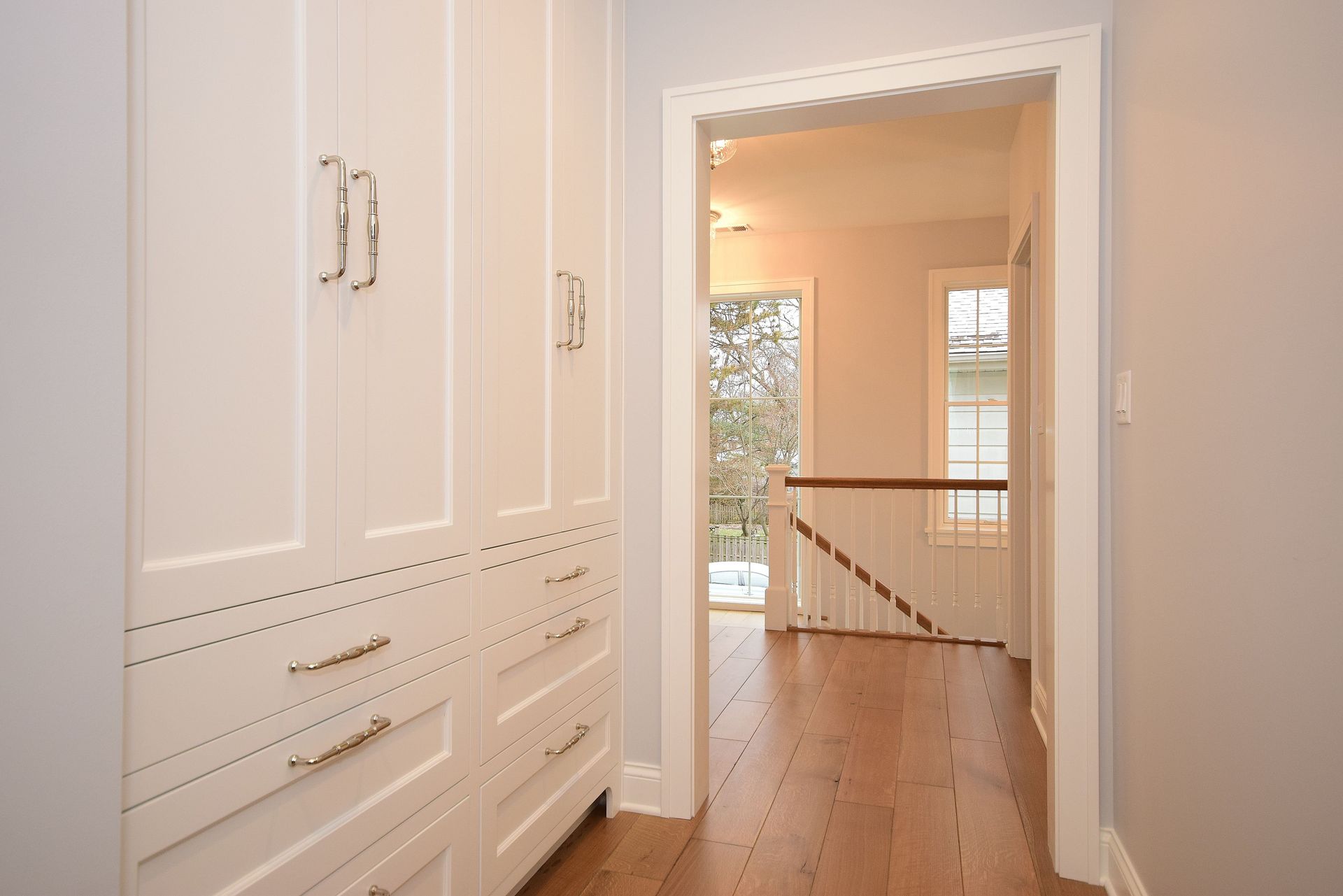 A hallway with white cabinets and drawers leading to a staircase.