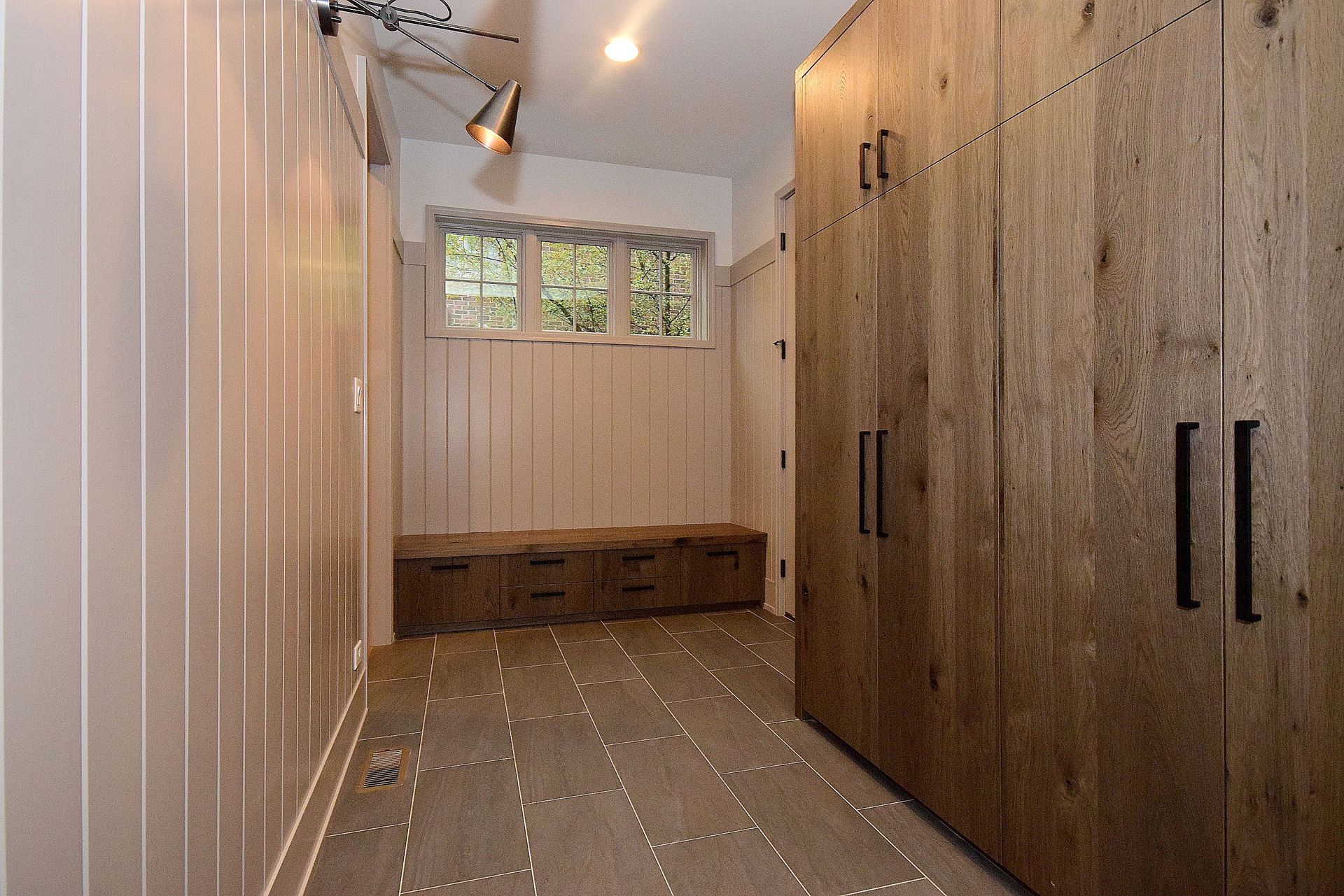 A long hallway with lots of wooden cabinets and a window.