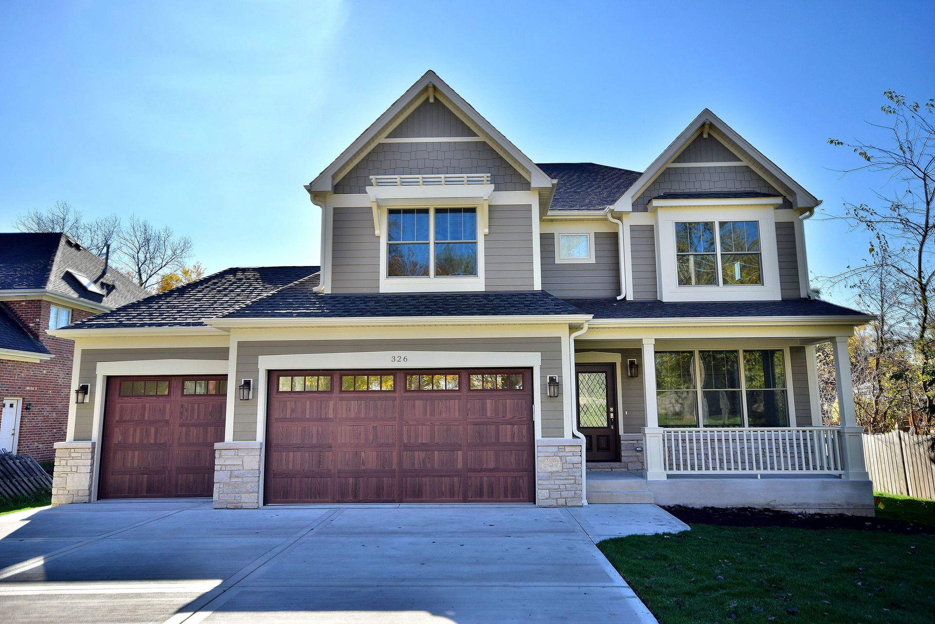 A large house with two garages and a porch on a sunny day.