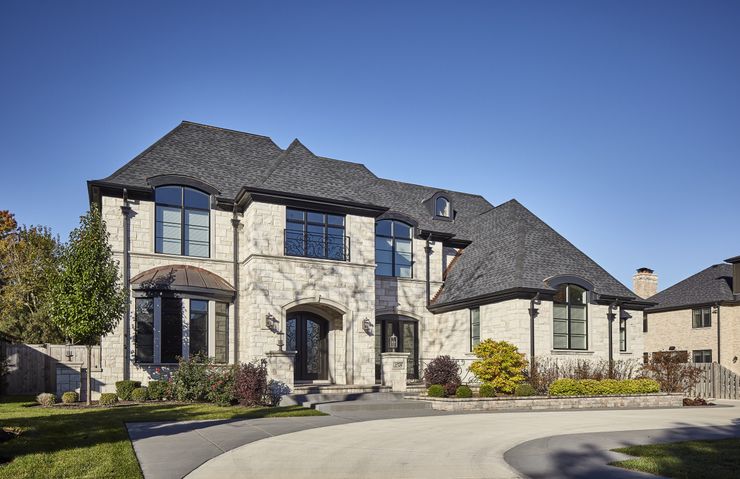 A large white house with a black roof is sitting on top of a lush green hillside.