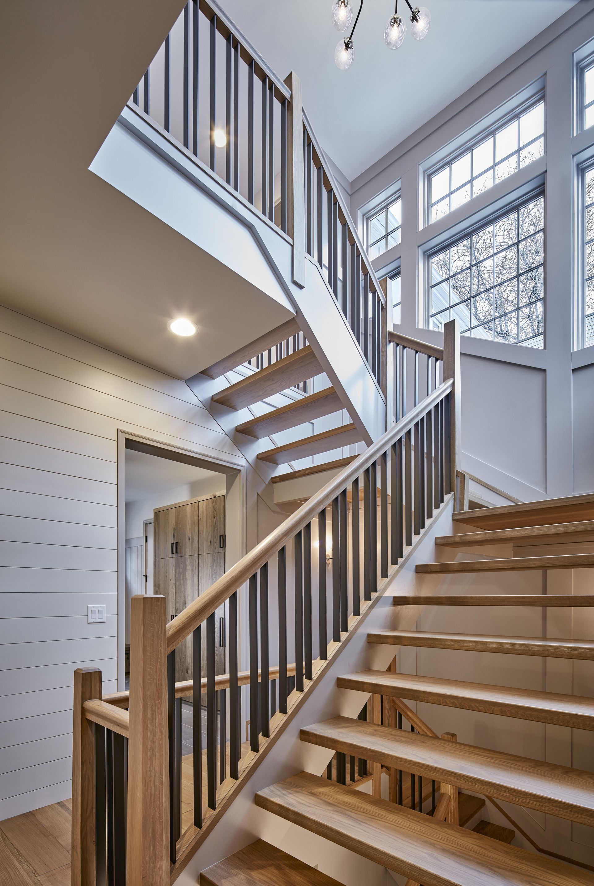 A wooden staircase with a metal railing in a house with lots of windows.