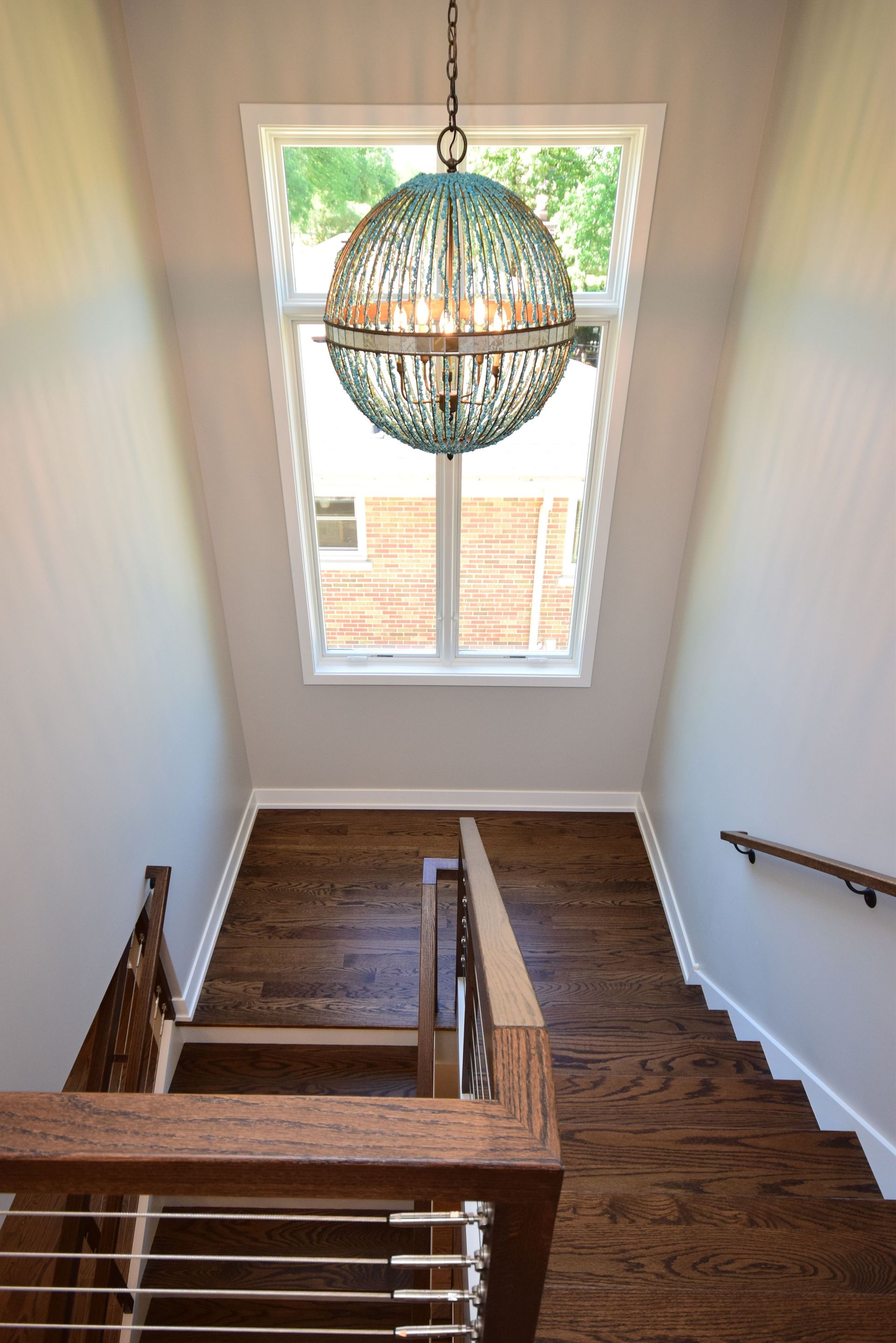A staircase with a chandelier hanging from the ceiling and a window.