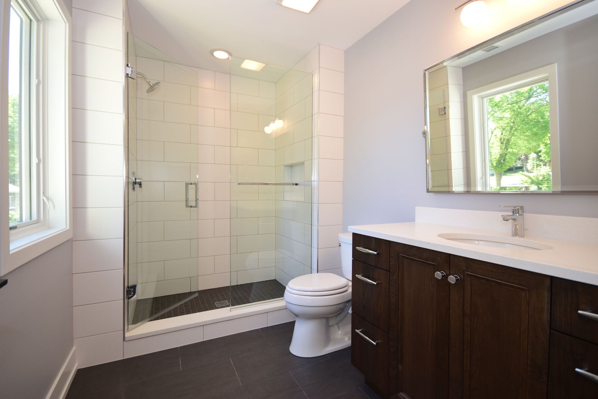 A bathroom with a toilet , sink , mirror and walk in shower.