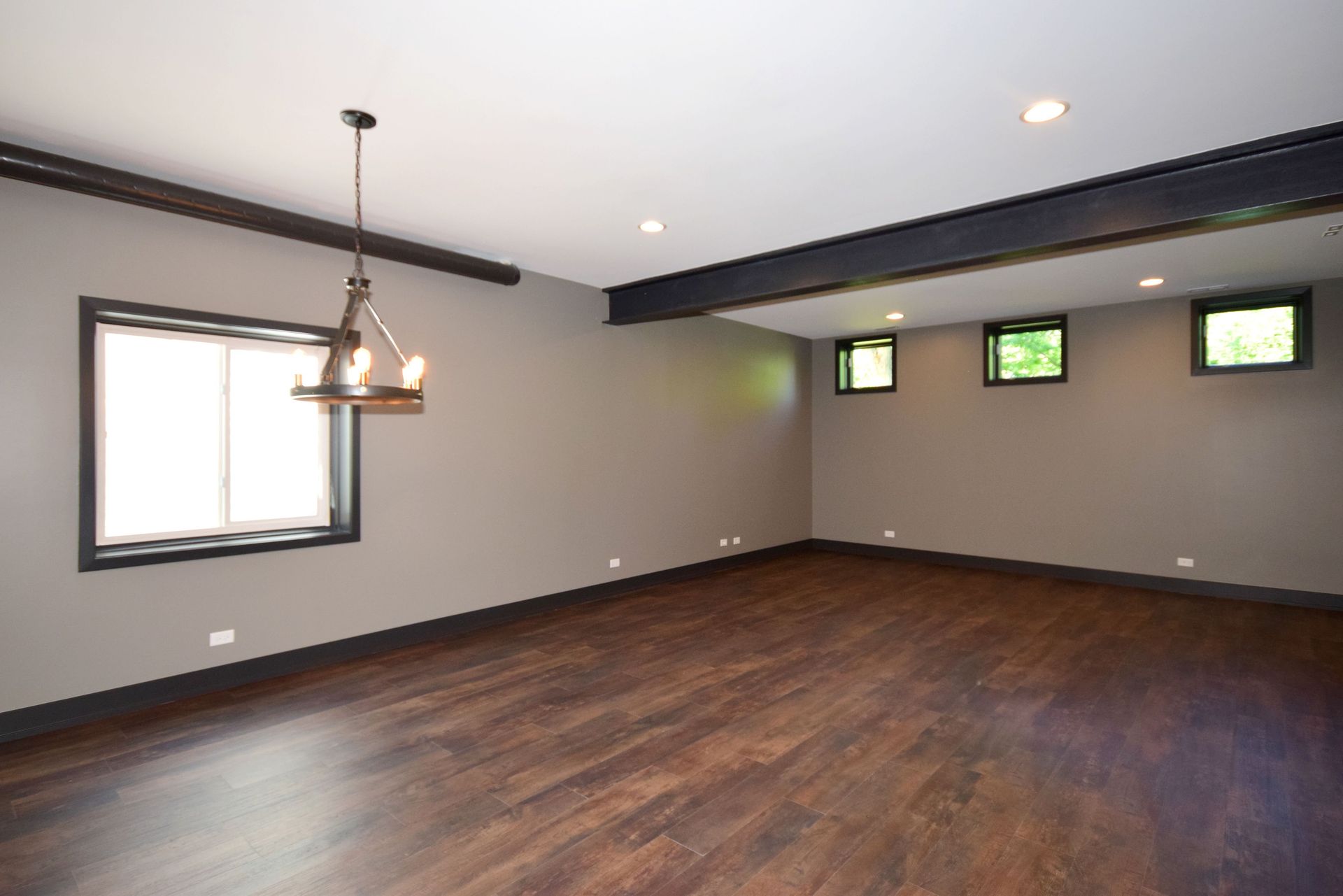 An empty room with hardwood floors and a chandelier hanging from the ceiling.