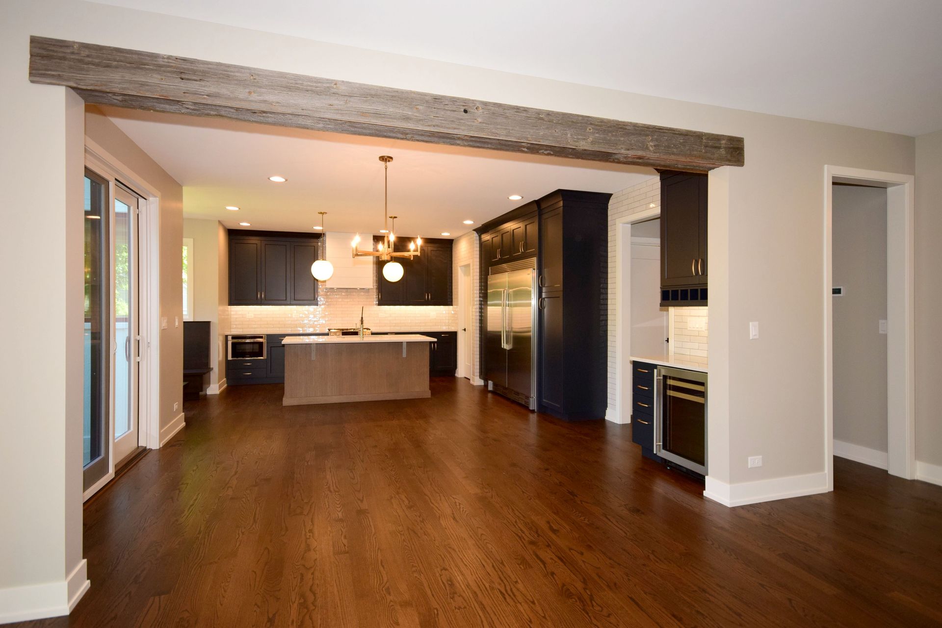 A large empty room with hardwood floors and a kitchen in the background.