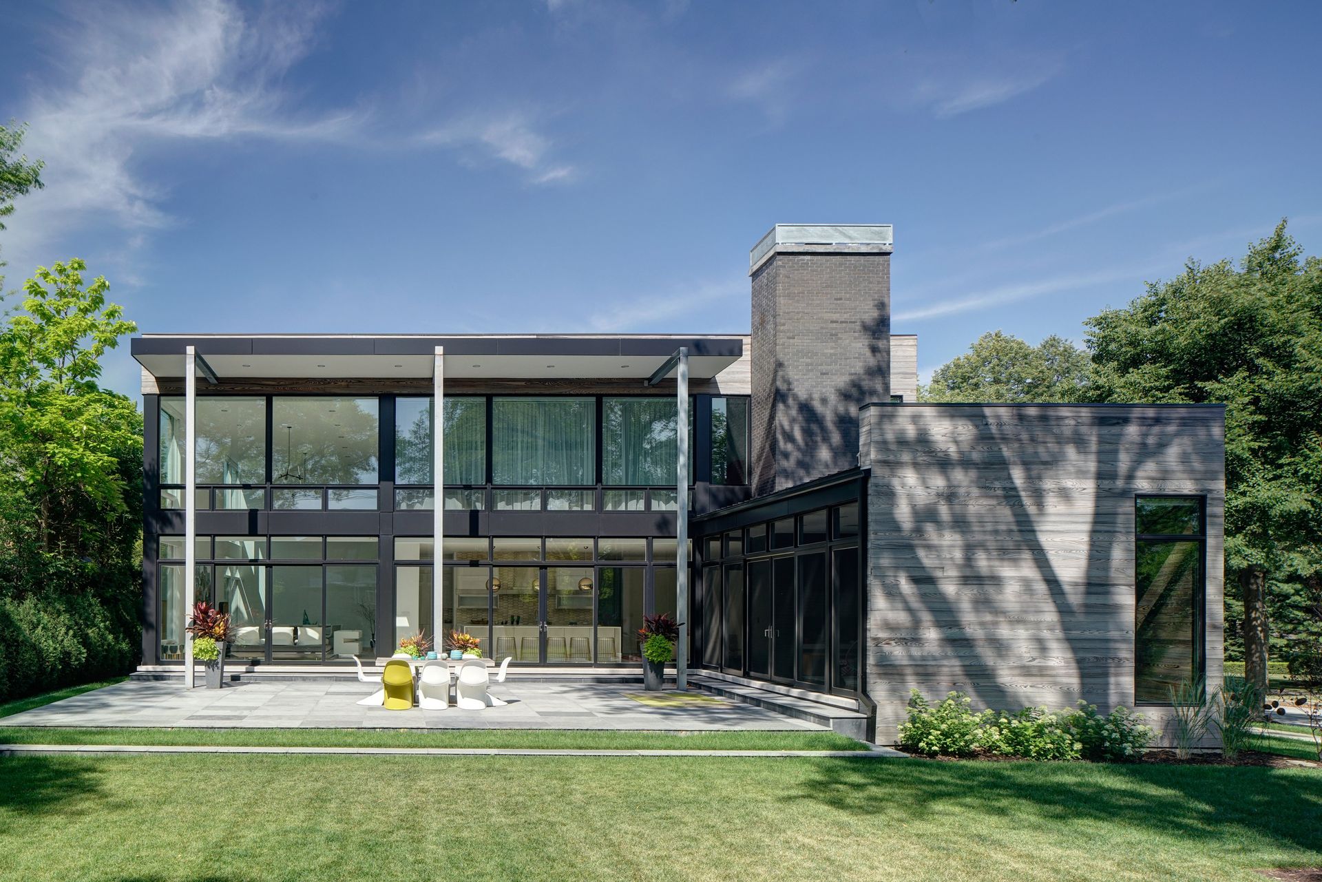 A large modern house with a lot of windows is sitting on top of a lush green lawn.