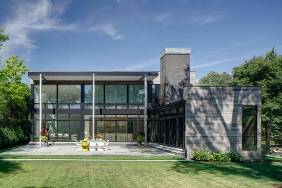A large modern house with a lot of windows is sitting on top of a lush green lawn.
