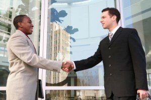 Two men are shaking hands in front of a building.