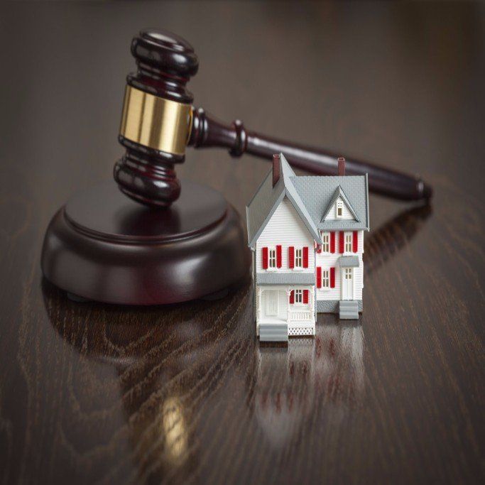 A judge 's gavel and a model house on a wooden table.