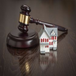 A judge 's gavel and a model house on a wooden table.